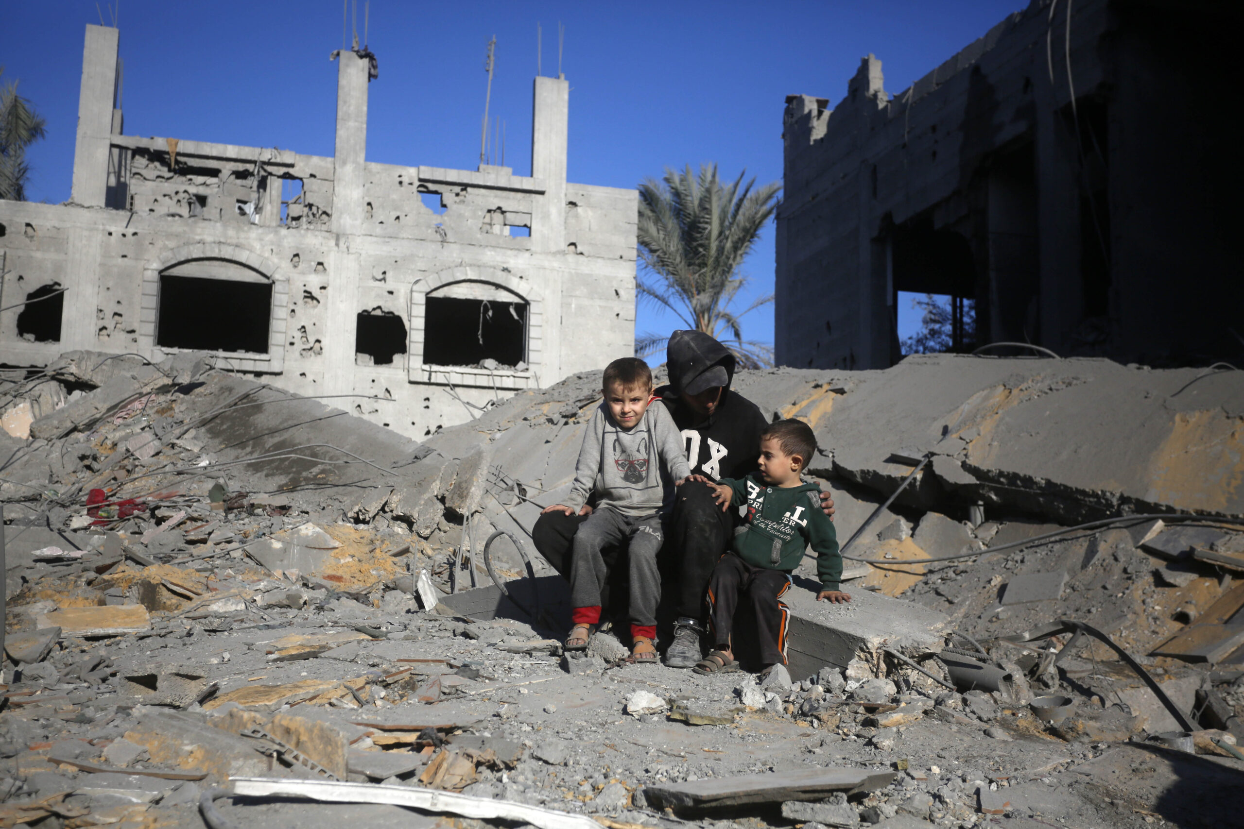 Adulto sentado junto a dos niños entre los escombros en Gaza